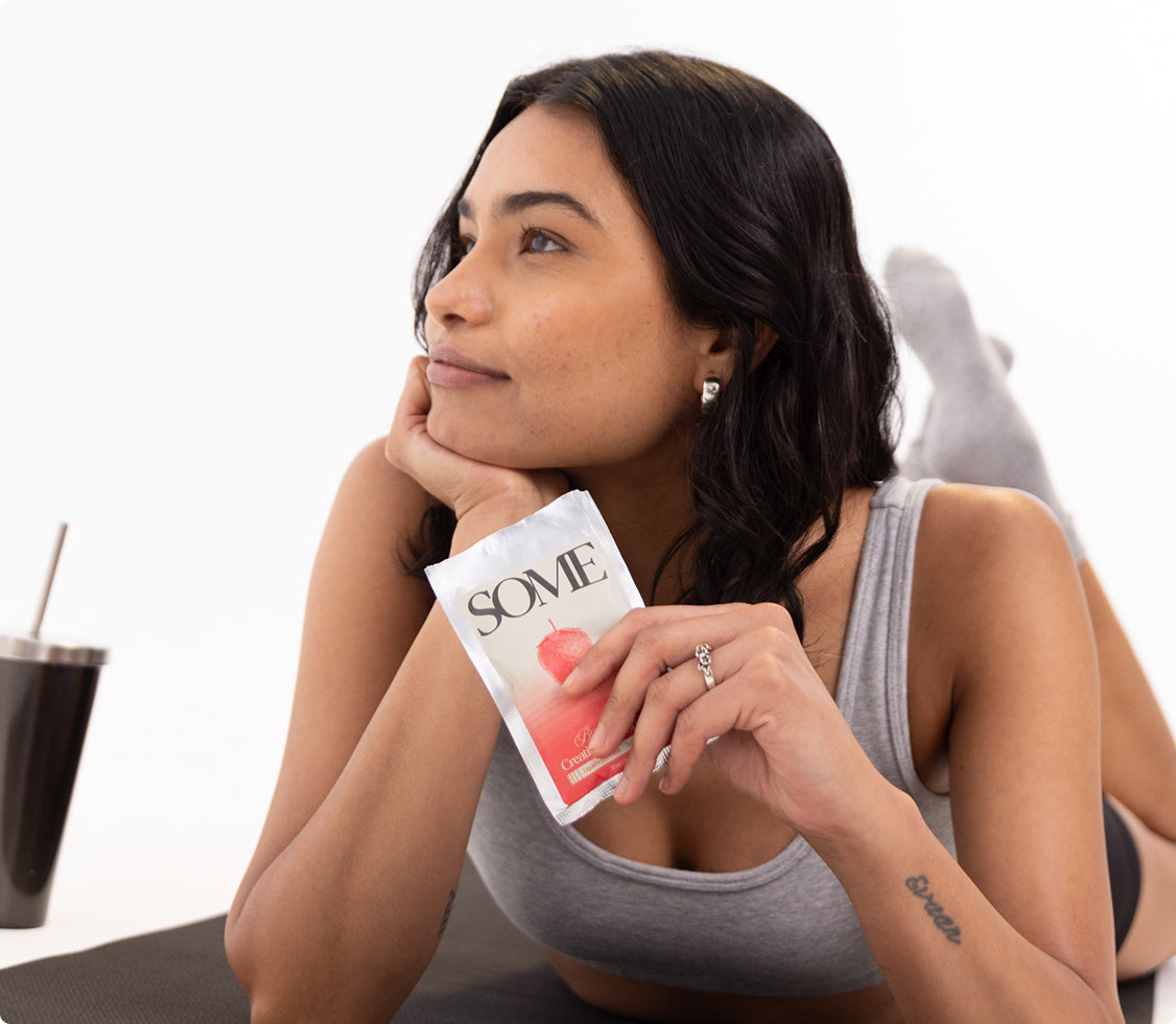 Woman relaxing on a yoga mat holding a SOME creatine sachet